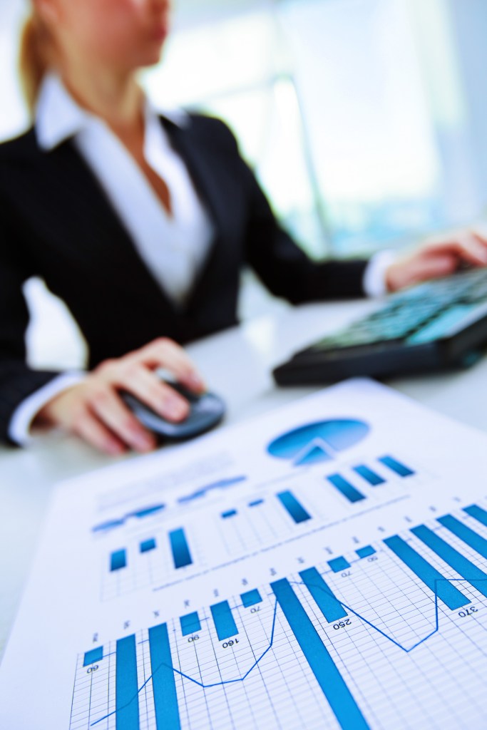 Woman on computer blurred and in focus is a chart in front of her hand, which is on a computer mouse. Mission Critical: A Practical Guide to Revenue Cycle Management for Rural and Community Hospitals | Community Hospital Corporation (CHC)